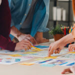 Photo showing arms and hands of people working together on charts laid flat on a table